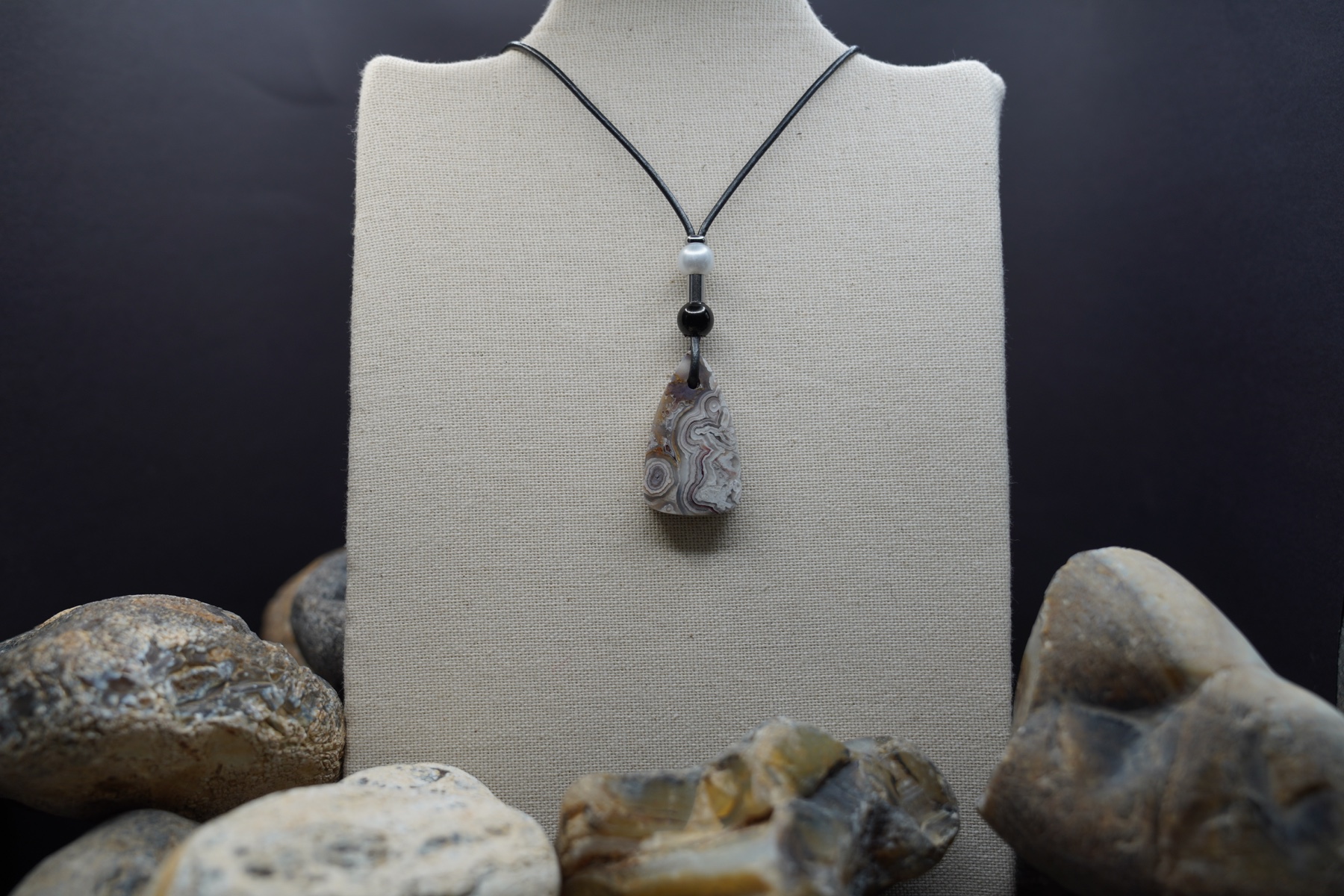 Handmade stone pendant necklace displayed with river rocks